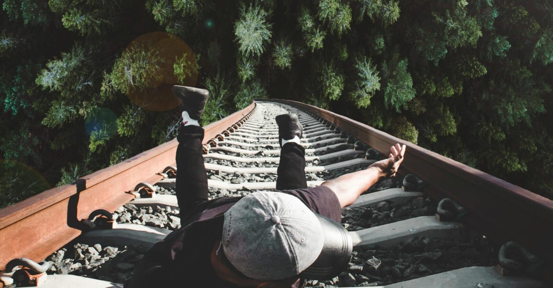 A man poses daringly over train tracks with a forest view.